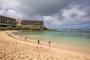A beach with a modern building, clear waters, and a cloudy sky. - Beach Cozy North Shore Turtle Bay Condo (Kahuku)
