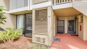 A residential building with a number '67' on the door, a sliding glass door entrance, and a small outdoor area with plants.