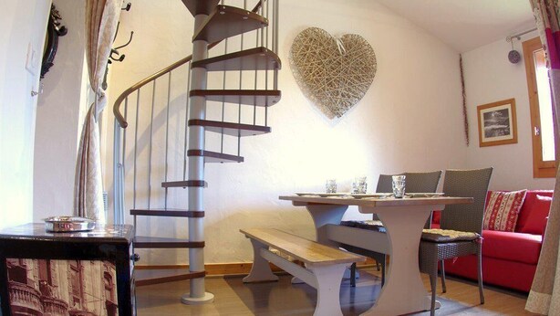 A cozy living room with a spiral staircase, a heart-shaped wall decoration, a red sofa, and a wooden table.