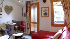 A cozy room with a red sofa, a dining table with chairs, a heart-shaped wall decoration, and a window with curtains.