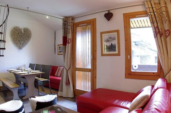 A cozy room with a red sofa, a dining table with chairs, a heart-shaped wall decoration, and a window with curtains. - 90m from shops, 6th floor, view resort, balcony, ski locker, 37m², Valmorel (Valmorel)