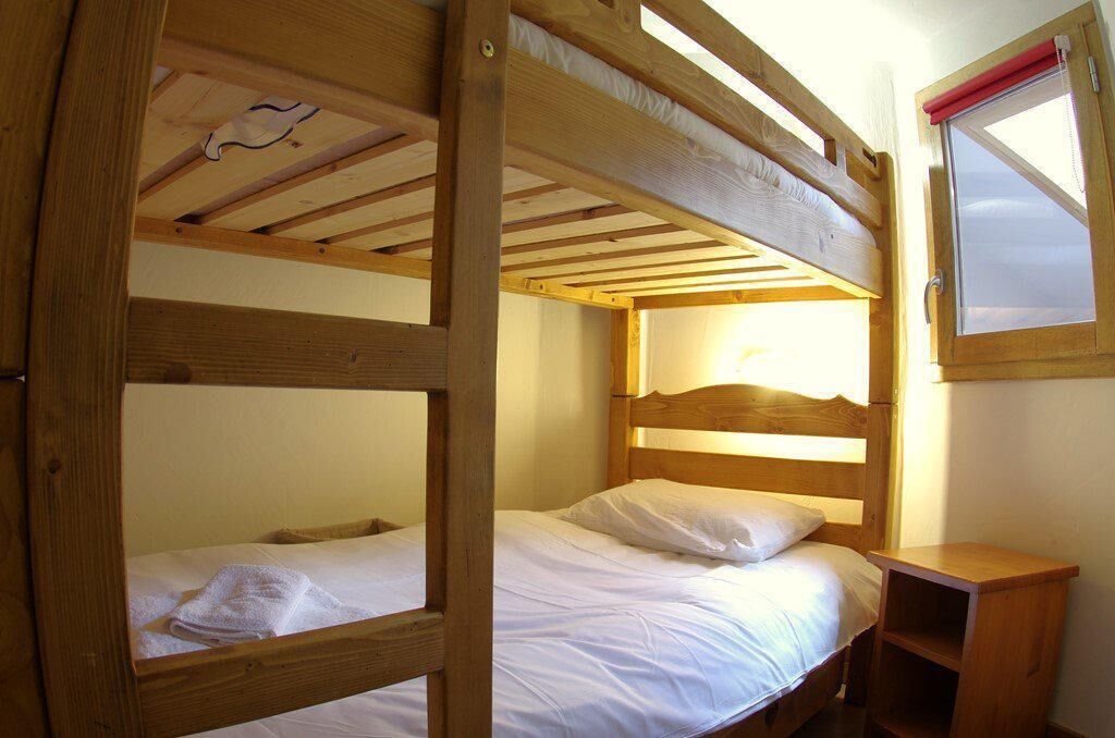 A bunk bed room with a wooden headboard, a small wooden nightstand, and a window with a red blind.