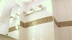 A bathroom with a white vessel sink, wooden shelves, and a tiled shower area.