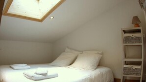 A bedroom with a skylight, a bed with white linens, and a bedside table with a lamp.