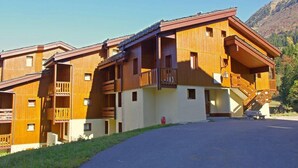 A multi-story wooden chalet with balconies, a ski lift, and a mountain backdrop.
