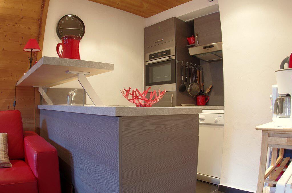 Une cuisine compacte dot ée d’appareils électroménagers modernes, d’une chaise rouge et d’une sculpture abstraite rouge originale.