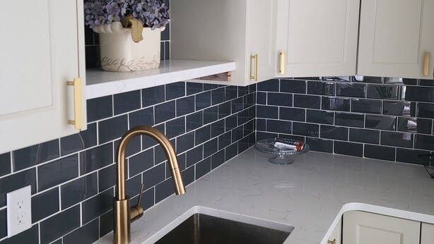 A kitchen with white cabinets, a black tiled backsplash, a stainless steel sink, and a gold faucet. - French Country Style Main Floor  in the heart of Lethbridge (Lethbridge)