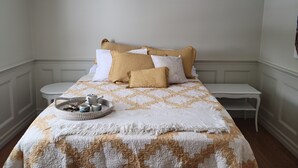 A neatly made bed with a patterned bedspread, a bedside table with a tray of tea and cups, and a wall-mounted picture. - French Country Style Main Floor  in the heart of Lethbridge (Lethbridge)