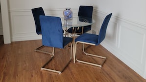 A dining area with a glass table surrounded by four blue chairs, a chandelier, and a framed picture on the wall. - French Country Style Main Floor  in the heart of Lethbridge (Lethbridge)