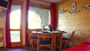 A cozy room with a wooden interior, a dining table set for two, and a window with red curtains. - 5m from ski slopes, 4th floor, terrace, ski locker, 24m², Valmorel (Valmorel)