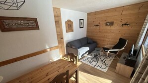 A cozy living area with a wooden dining table, a sofa, and a chair. There are wall decorations and a wooden wall panel. - 5m from ski slopes, 1st floor, view ski slopes, balcony, tv, 31m², Valmorel (Valmorel)