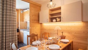 A wooden dining table set with plates, glasses, and cutlery, with a hanging light fixture above. - 5m from ski slopes, 1st floor, view ski slopes, balcony, tv, 31m², Valmorel (Valmorel)