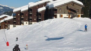 Ein Skigebiet mit mehrstöckigen, schneebedeckten Gebäuden, Skipisten und Skifahrern.
