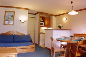 Una habitación acogedora con un sofá de madera, una mesa de comedor con sillas, un microondas y una pequeña cocina.