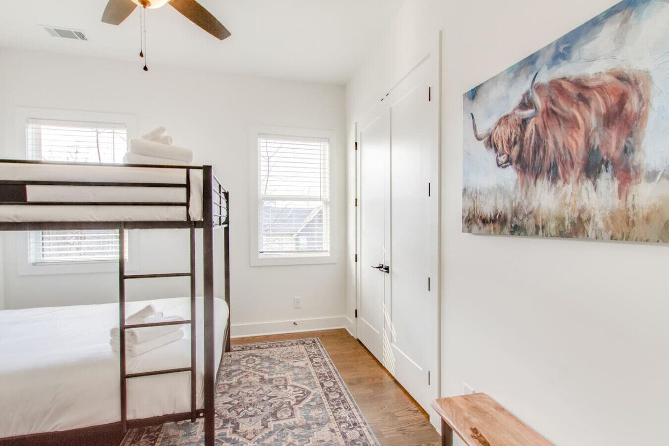 A bunk bed room with a ceiling fan, a painting of a bull, and a patterned rug.