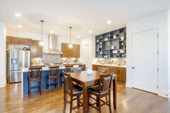 A modern kitchen with a central island, wooden chairs, and built-in shelving.