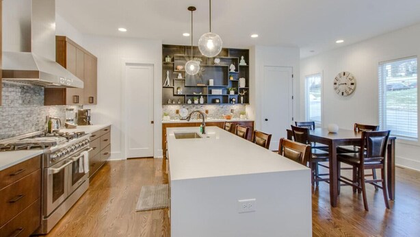 Una cocina moderna con una isla central, armarios de madera y un comedor con una mesa grande y sillas.