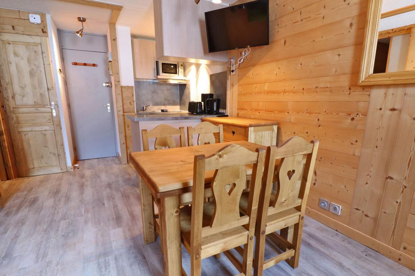 Un intérieur en bois comprenant une table et des chaises, un coin cuisine avec un four à micro-ondes et un téléviseur fixé au mur.