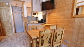 Ein Holzinnenraum mit Esstisch und Stühlen, einer Küchenzeile mit Mikrowelle und einem an der Wand befestigten Fernseher.