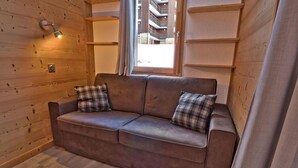 Ein Holzinnenraum mit einem braunen Ledersofa, zwei karierten Kissen, einer Wandleuchte und einem Fenster mit Vorhängen.