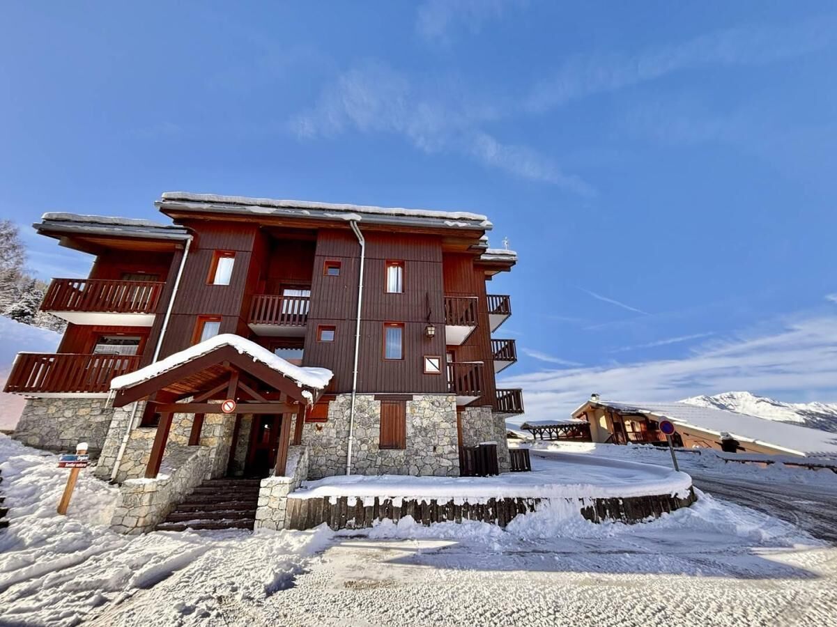 Un bâtiment en bois à plusieurs étages, doté de balcons, d’une fondation en pierre et d’une entrée recouverte de neige.