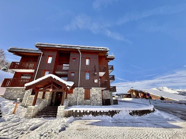 A multi-story wooden building with balconies, stone foundation, and a snow-covered entrance.