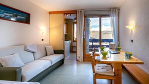 Um quarto acolhedor com sofá, uma mesa de jantar com cadeiras e vista para uma paisagem montanhosa através de grandes janelas.