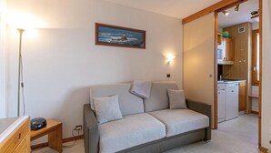 Un soggiorno accogliente con un divano, un quadro e una cucina visibile attraverso una porta aperta.