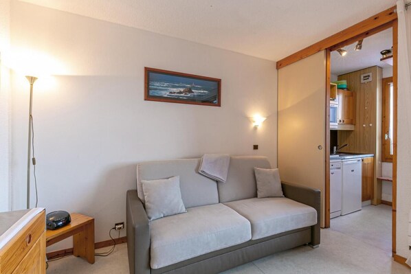 Ein gemütliches Wohnzimmer mit einer Couch, einem Bild und einer durch eine offene Tür einsehbarer Küche.