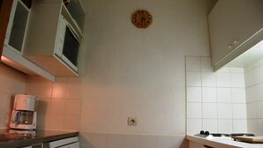 Una cocina con armarios blancos, un reloj en la pared y una cafetera sobre la encimera.
