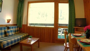 Una sala de estar acogedora con un sofá a cuadros, una mesa de madera, un televisor y un comedor con sillas y una mesa dispuesta para dos.