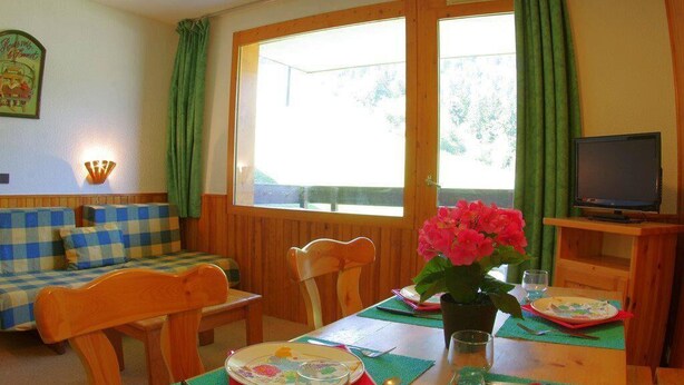 Una habitación acogedora con una mesa de madera dispuesta para comer, un sofá y un televisor.
