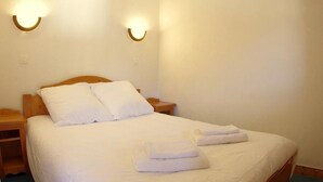 Een netjes opgemaakt bed met witte lakens en twee handdoeken gevouwen aan het voeteneinde.