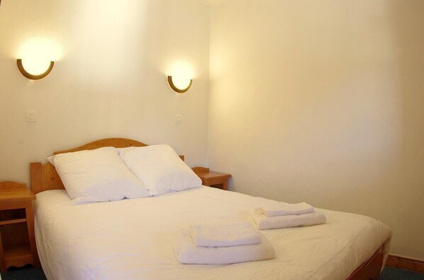 Een netjes opgemaakt bed met witte lakens en twee handdoeken gevouwen aan het voeteneinde.