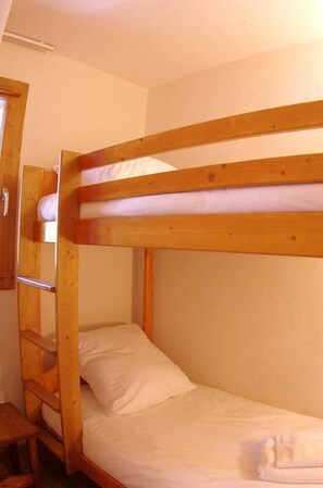 Een stapelbed met een houten ladder, een klein houten tafeltje en een effen muur.