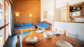 Een gezellige kamer met een houten plafond, een eettafel gedekt met borden en glazen, en twee blauwe banken.