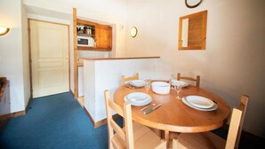 Een eetruimte met een ronde houten tafel voor vier personen, een keuken met houten kastjes, en een vloer met blauw tapijt.