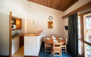 Een compacte keuken met een eethoek, houten kastjes, een magnetron en een klok aan de muur.