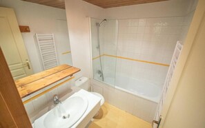 Een badkamer met een wit wastafel, houten opbergmeubel, een douchecabine met glazen wanden en een bad.