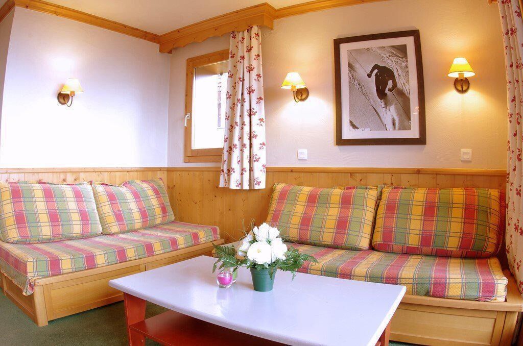 A cozy room with two plaid sofas, a small table with a vase of flowers, and wall-mounted lamps.
