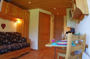 A cozy room with a wooden ceiling, a sofa, a dining table with chairs, and a wooden cabinet. - 1st floor, view ski slopes, balcony, 12m², Valmorel (Valmorel)