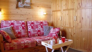 A wooden cabin interior with a red and white patterned sofa, a wooden cabinet, and a small table with a mug and a red cup. - 5m from ski slopes, 1st floor, view valley, balcony, tv, 24m², Valmorel (Valmorel)
