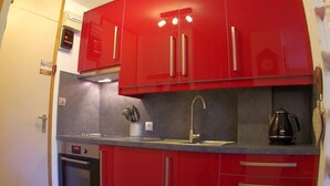 A compact kitchen with red cabinets, a stainless steel oven, a sink, and a kettle. - 5m from ski slopes, 1st floor, view valley, balcony, tv, 24m², Valmorel (Valmorel)