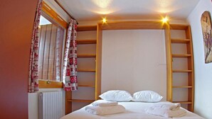 A bedroom with a bed, white linens, a radiator, and wooden shelves. - 1st floor, view mountain, tv, 24m², Valmorel (Valmorel)