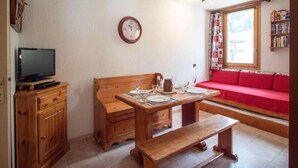 A cozy room with a wooden table set for dining, a red sofa, a television on a wooden cabinet, and a clock on the wall. - 1st floor, view mountain, tv, 24m², Valmorel (Valmorel)