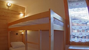 Habitación con literas, paredes de madera, una mesita de noche pequeña y una ventana con cortina estampada.