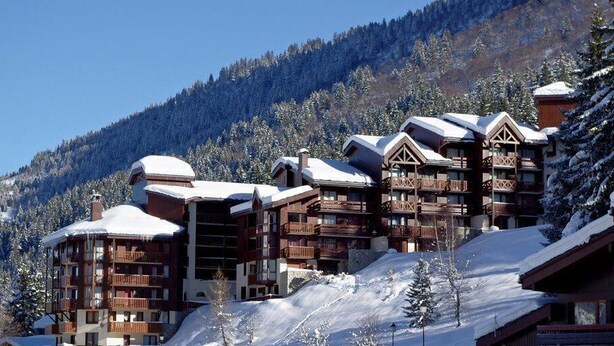 Un centro de esquí con edificios de madera, techos cubiertos de nieve y un paisaje montañoso.