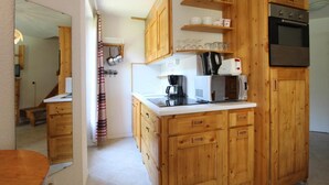 A compact kitchen with wooden cabinets, a microwave, a coffee maker, and a built-in oven. - 100m from ski slopes, 3rd floor, balcony, tv, ski locker, 35m², Val Cenis (Lanslevillard)