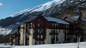 A multi-story hotel with a red and beige facade, balconies, and a snowy mountain backdrop. - 100m from ski slopes, 3rd floor, balcony, tv, ski locker, 35m², Val Cenis (Lanslevillard)