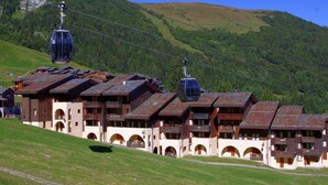 Un chalet de montagne composé de plusieurs bâtiments de style chalet, doté d’un téléphérique et surplombant une colline verdoyante.